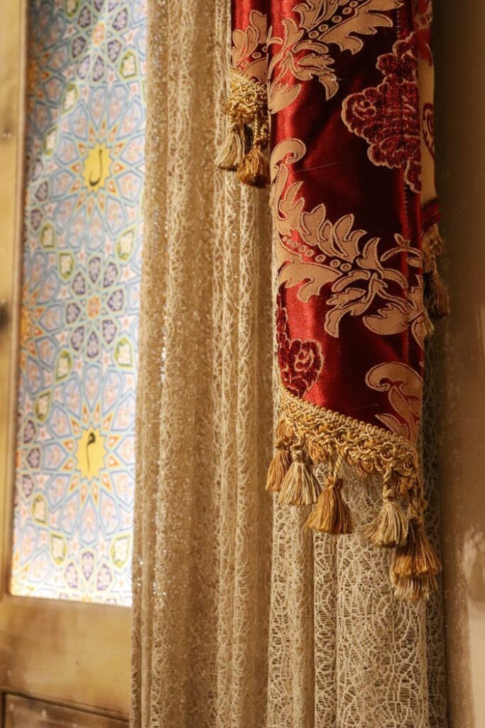 pexels-photo-34703524 Elegant lace curtain with ornate red fabric beside colorful stained glass window.